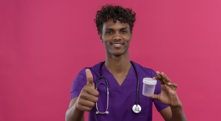 a happy young handsome dark-skinned doctor with curly hair wearing violet uniform with stethoscope showing thumbs up while holding plastic specimen jar on a pink background